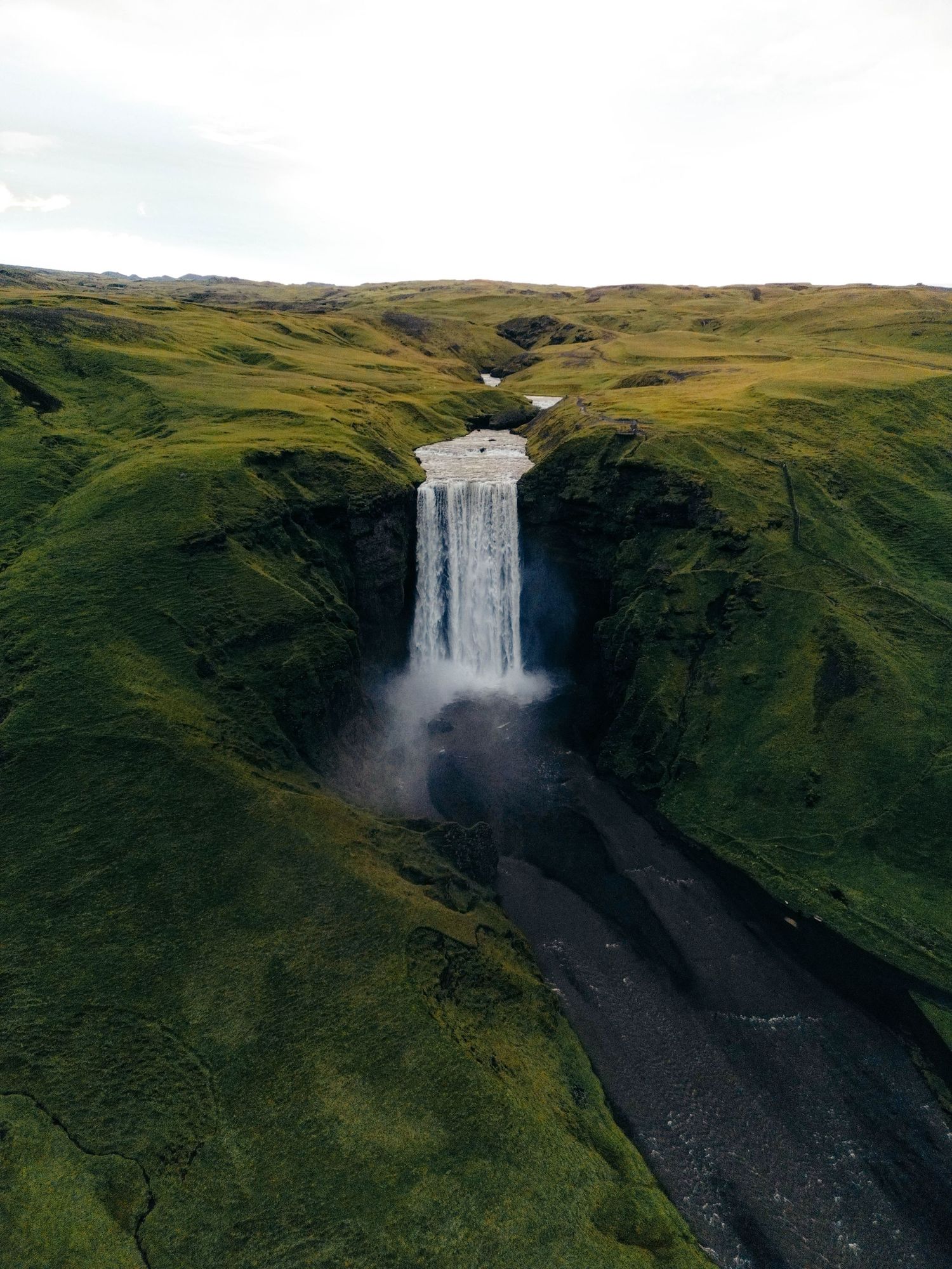 Majestic Skogafoss waterfall cascades down green cliffs in Iceland's rugged landscape during summer.