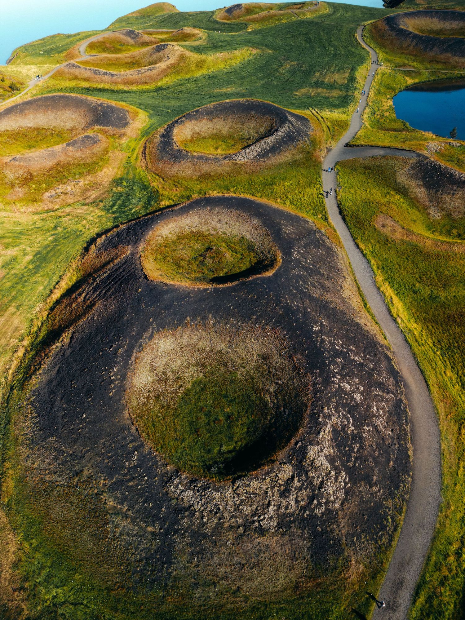 Aerial view of winding roads through green volcanic craters and ancient lava fields in Iceland's rugged landscape.