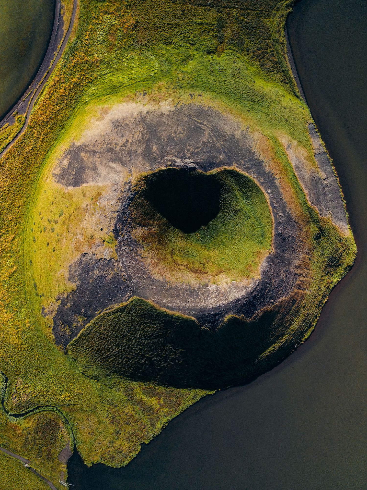 Aerial view of a volcanic crater with moss-covered edges and dark center showing multiple stages of formation.