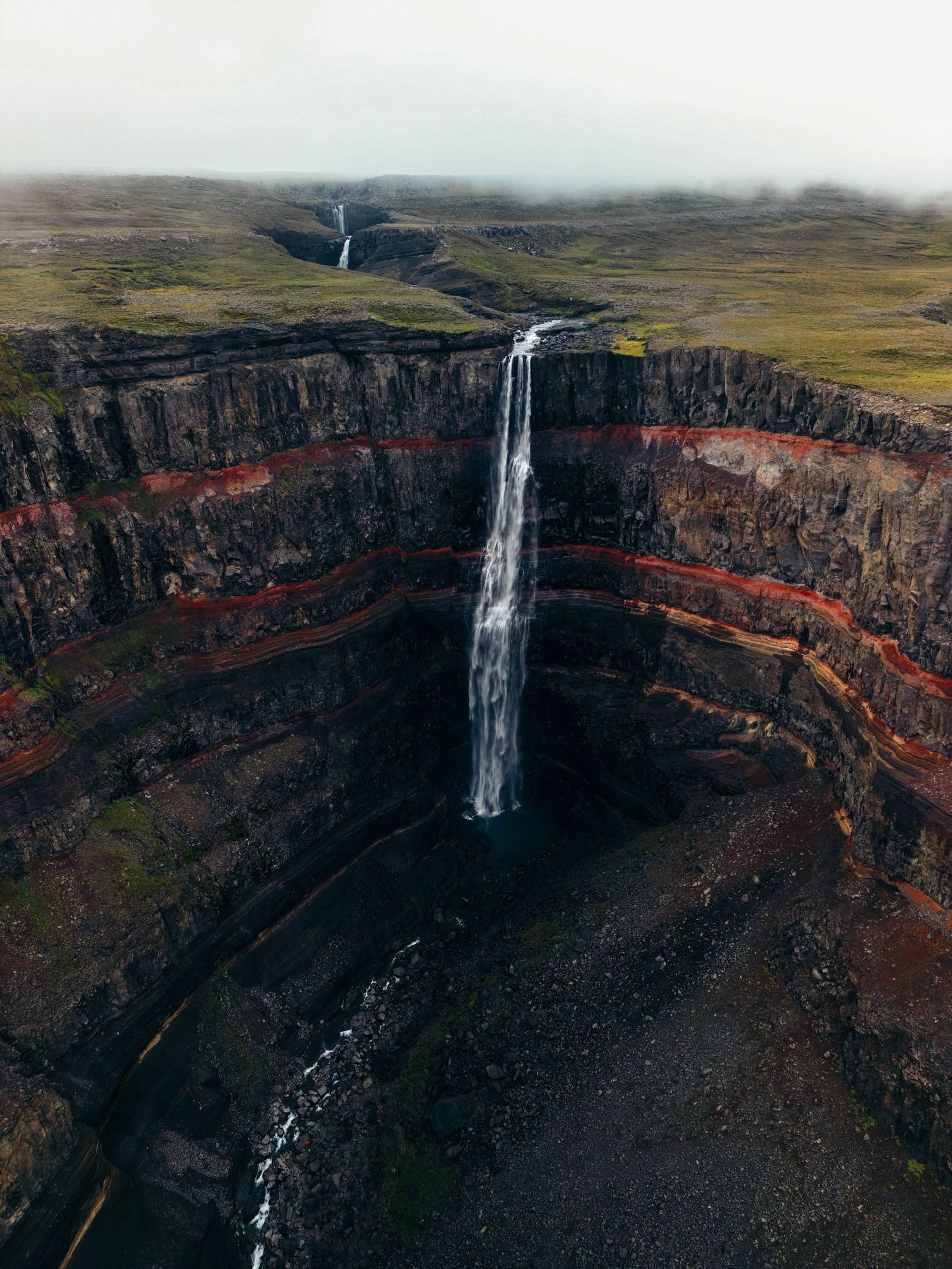 Dramatic waterfall cascading down steep volcanic cliffs in a remote mountainous landscape.