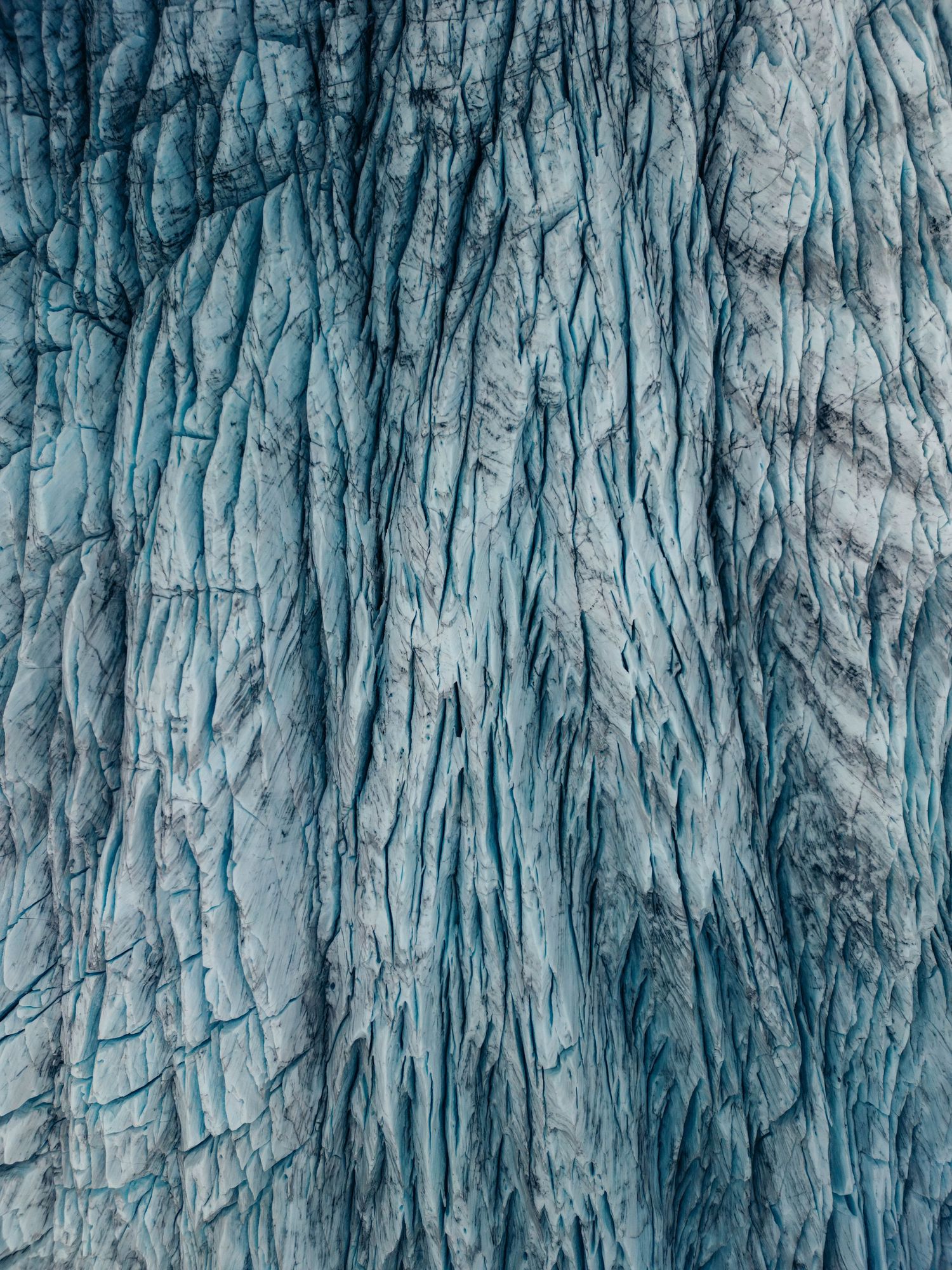 Abstract pattern of vertical blue and white ice formations creating a textured glacial surface in natural lighting.