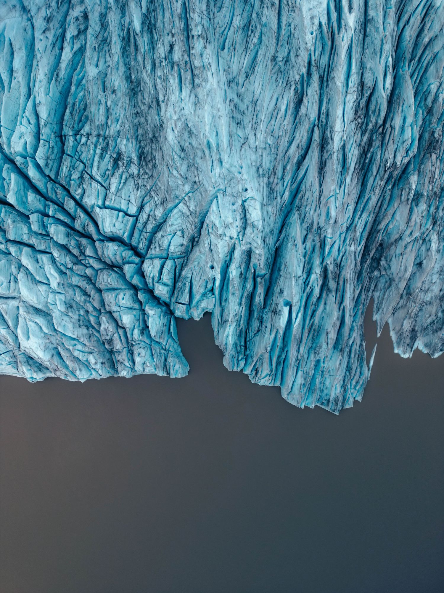 Dramatic blue glacial ice formations create a stunning natural wall above dark waters in a frozen landscape.