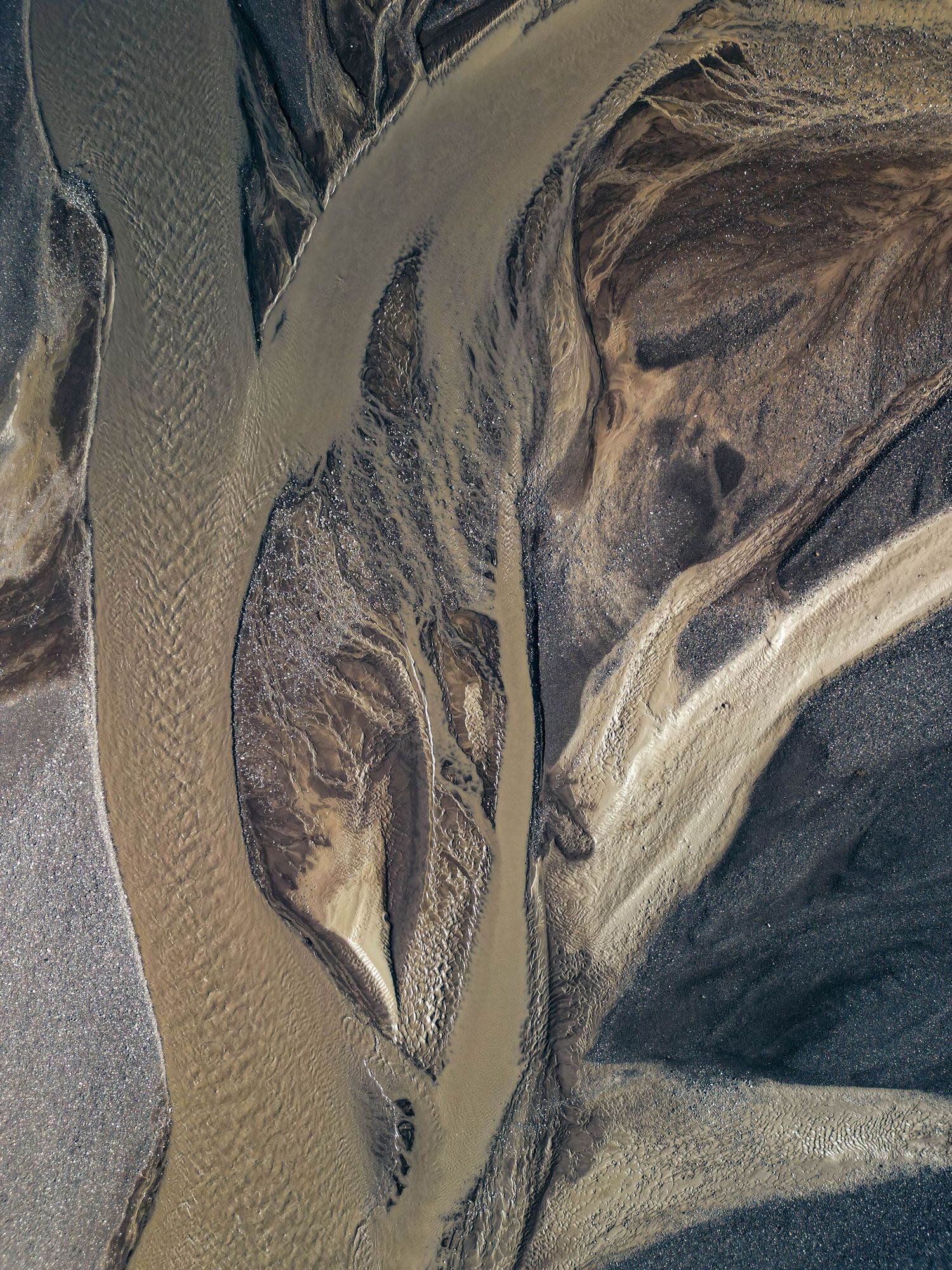 Aerial view of a winding river delta with sandy patterns and sediment creating abstract natural formations in brown tones.