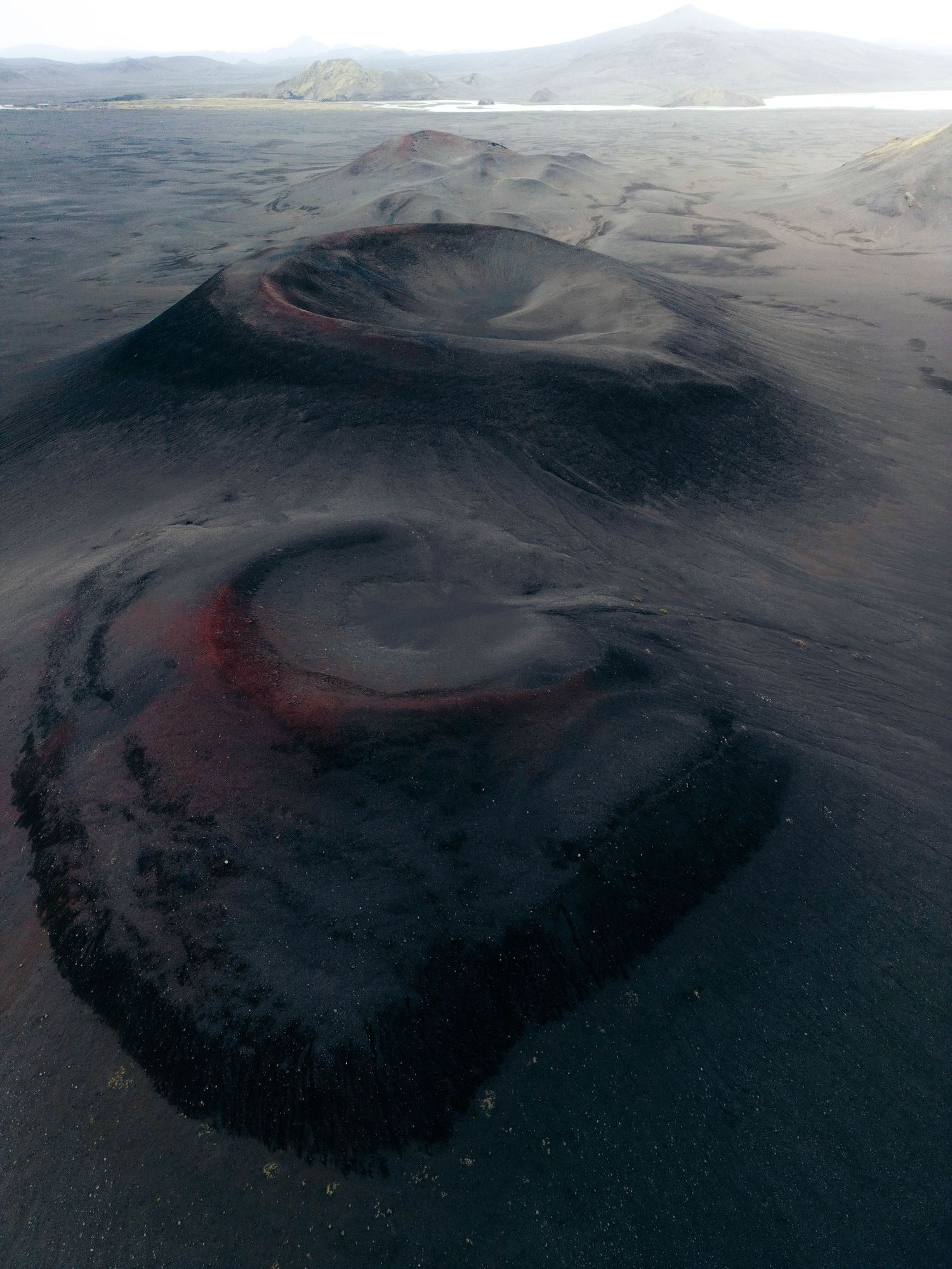 Aerial view of dark volcanic crater formations in a mountainous landscape showing multiple peaks and ridges.