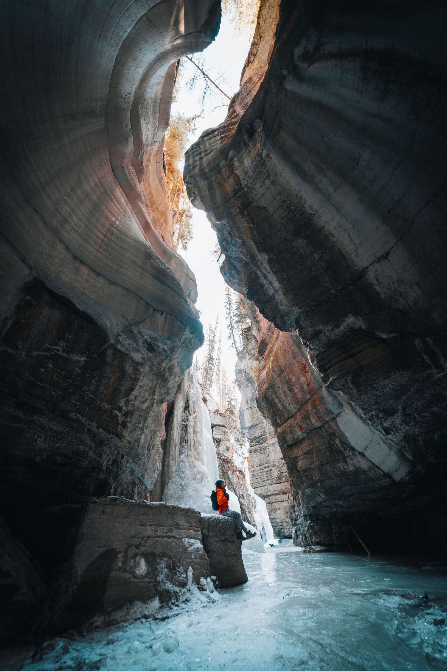 Dramatic view of a narrow canyon with turquoise water and red rock walls illuminated by natural light from above.