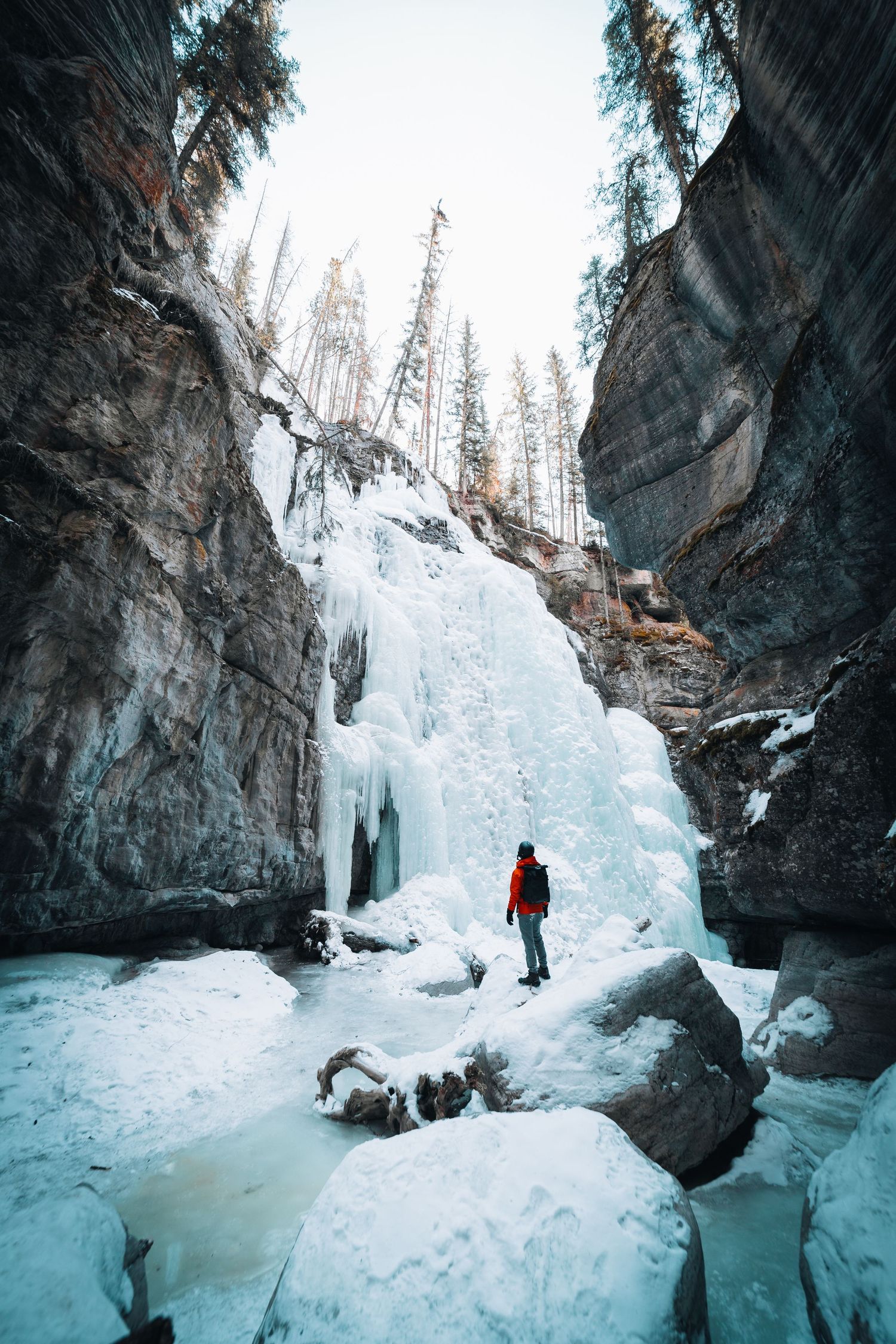 An adventurer explores a frozen canyon with massive ice formations and towering rock walls in winter.