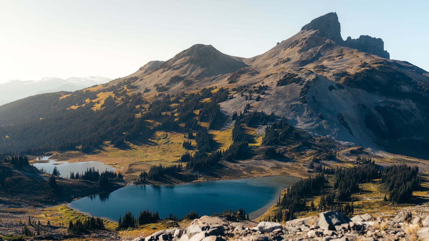 Mountain landscape with a pristine alpine lake nestled between rugged peaks and green meadows.