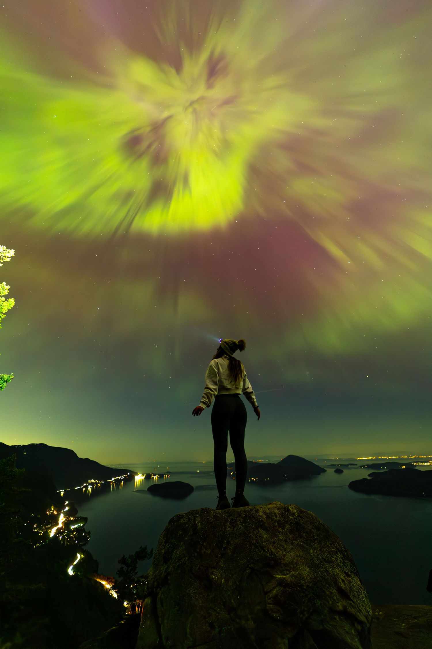 Dramatic green aurora borealis lights dance in the night sky over a silhouetted mountain landscape.