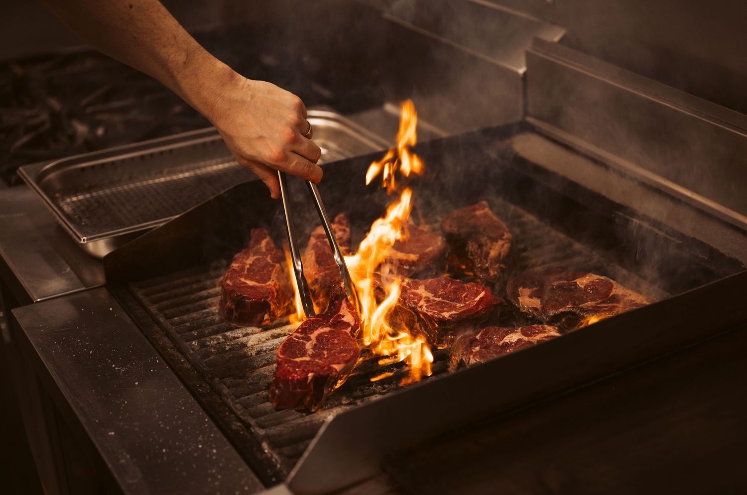 Hospitality kitchen photography capturing steak cooking over open flame in commercial restaurant kitchen