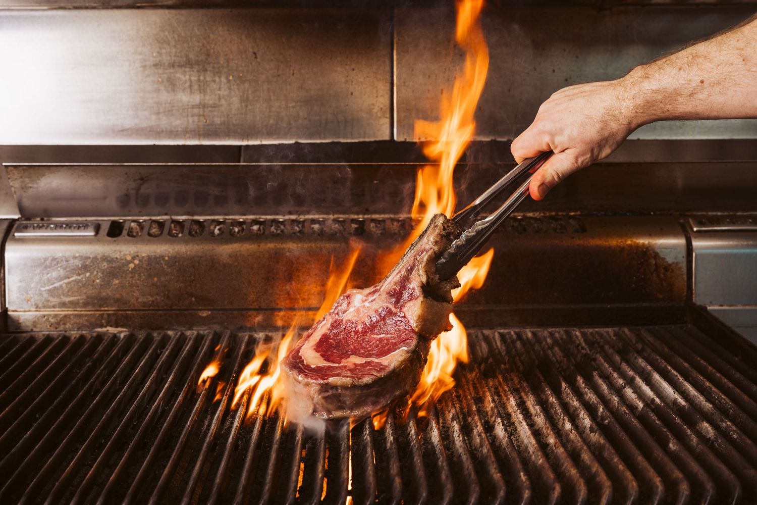 Commercial kitchen photography capturing steak cooking over open flame in hospitality venue