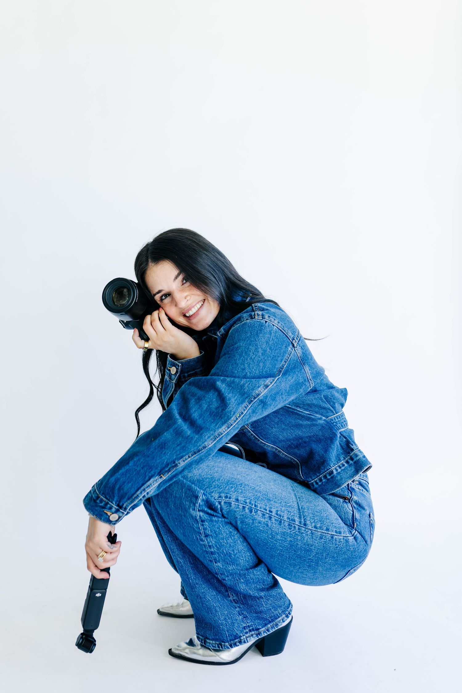 Woman in denim jacket holding tablet and adjusting white baseball cap.