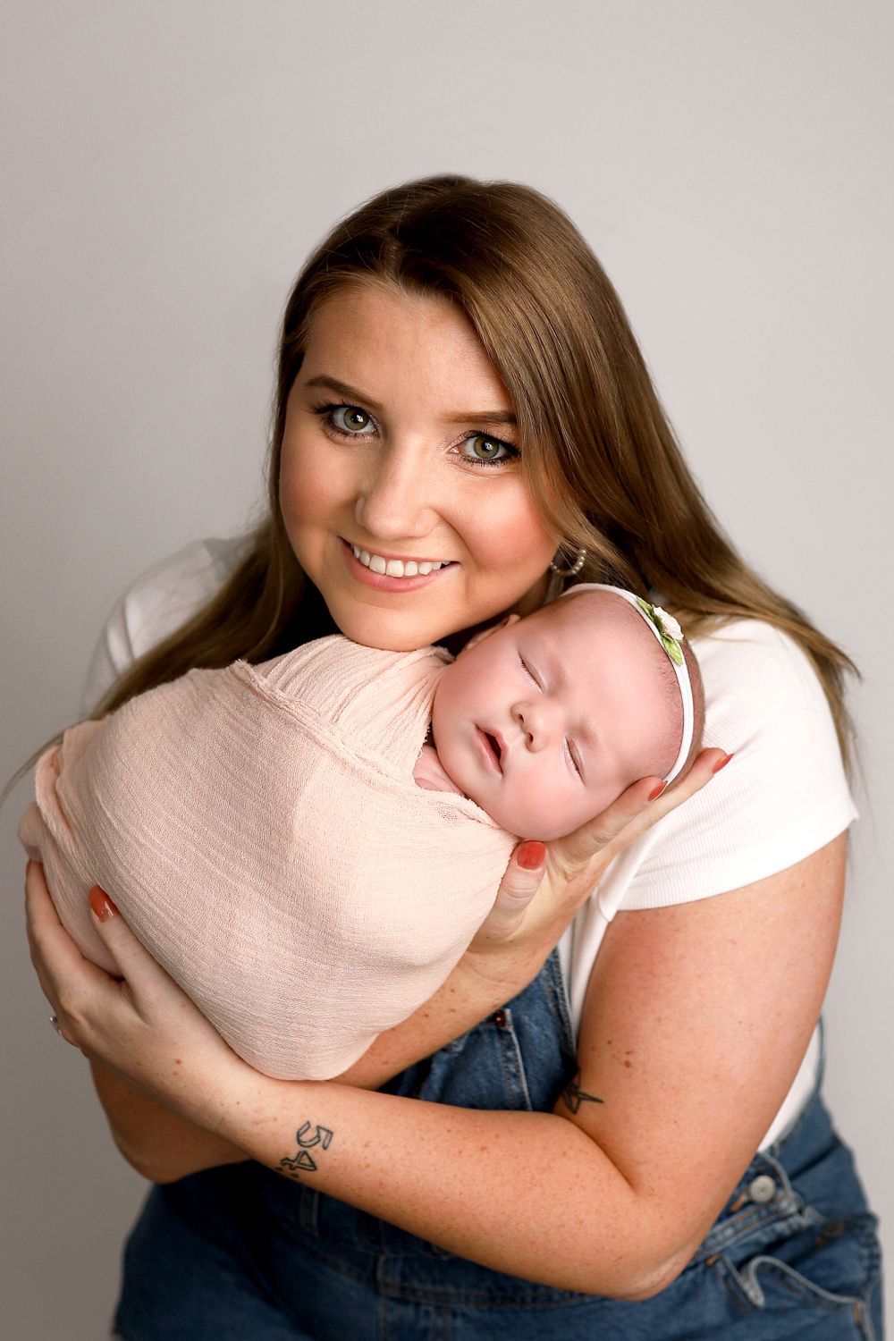 A loving mother wearing a white shirt cradles her sleeping baby swaddled in pink during a portrait session. Orem studio.