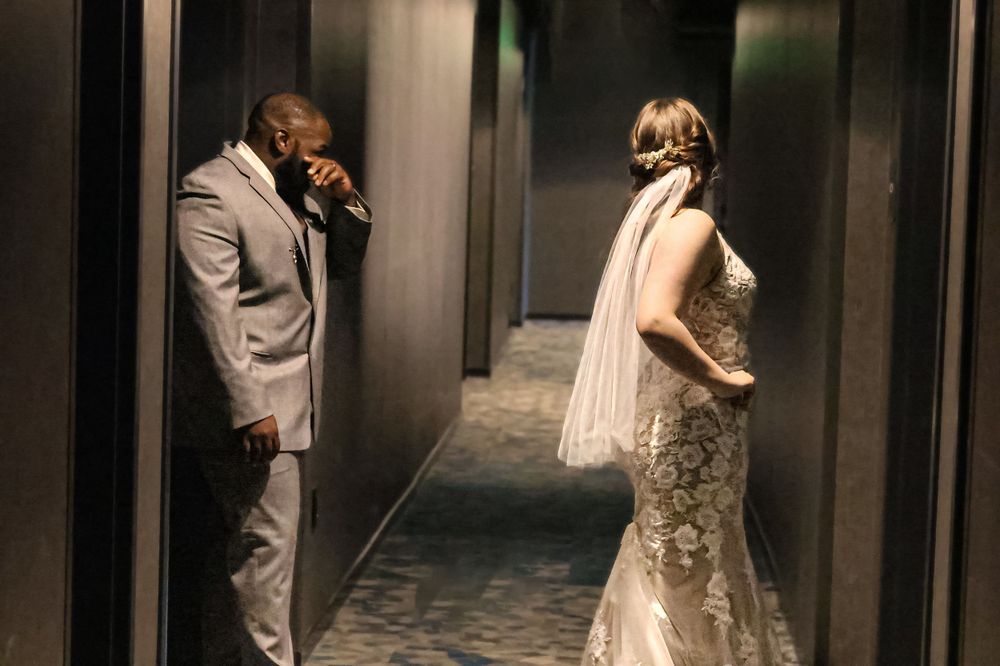 A romantic wedding photo of a couple in formal attire in a dramatic hallway setting.