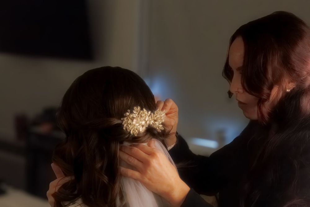 Wedding preparation scene with hair accessory being placed in dim lighting.