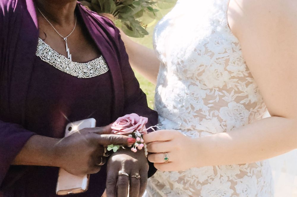 Detailed shot of hands exchanging rings with a lace wedding dress in frame.