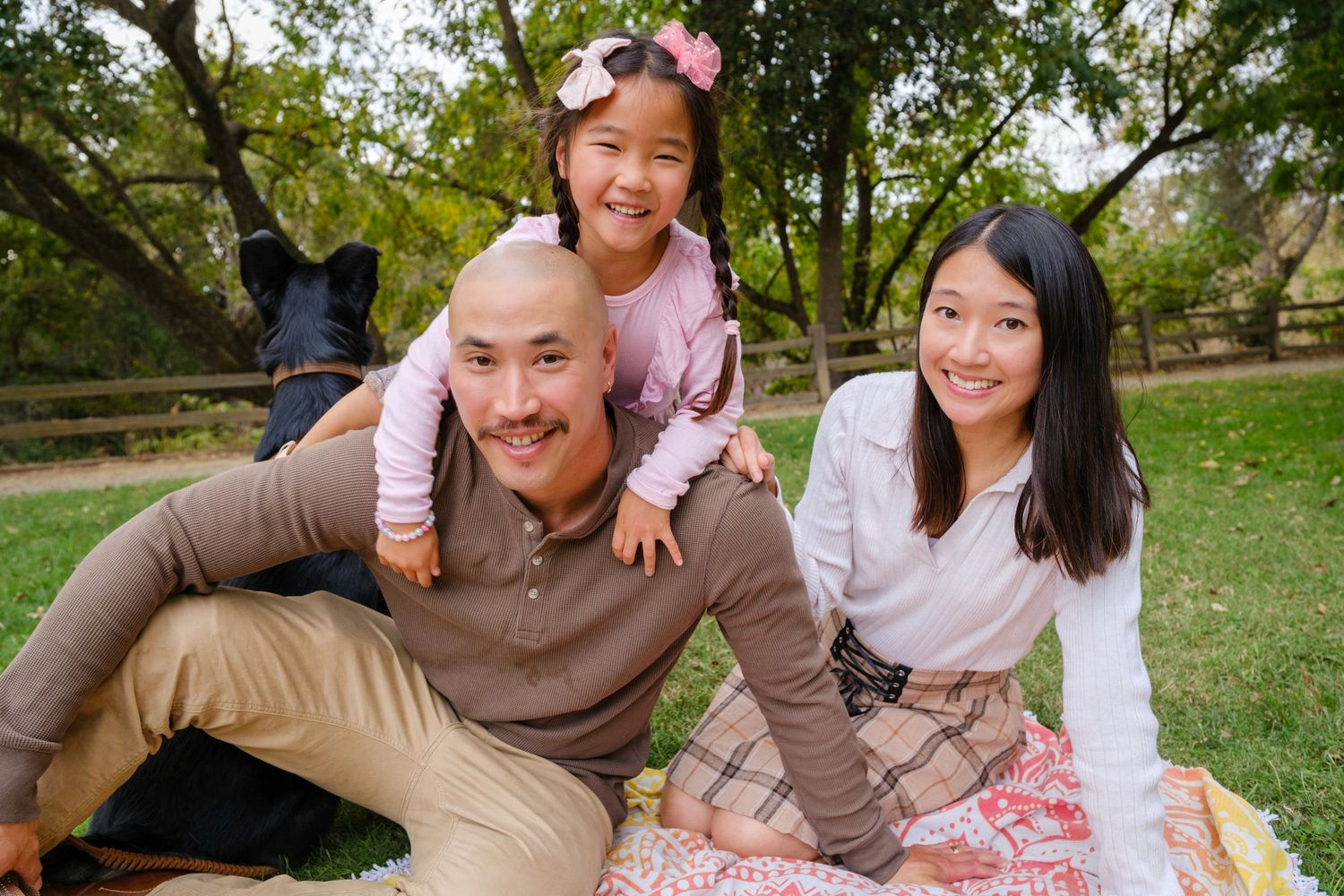 A family shares a joyful moment together while standing on a wooden bridge surrounded by green trees.