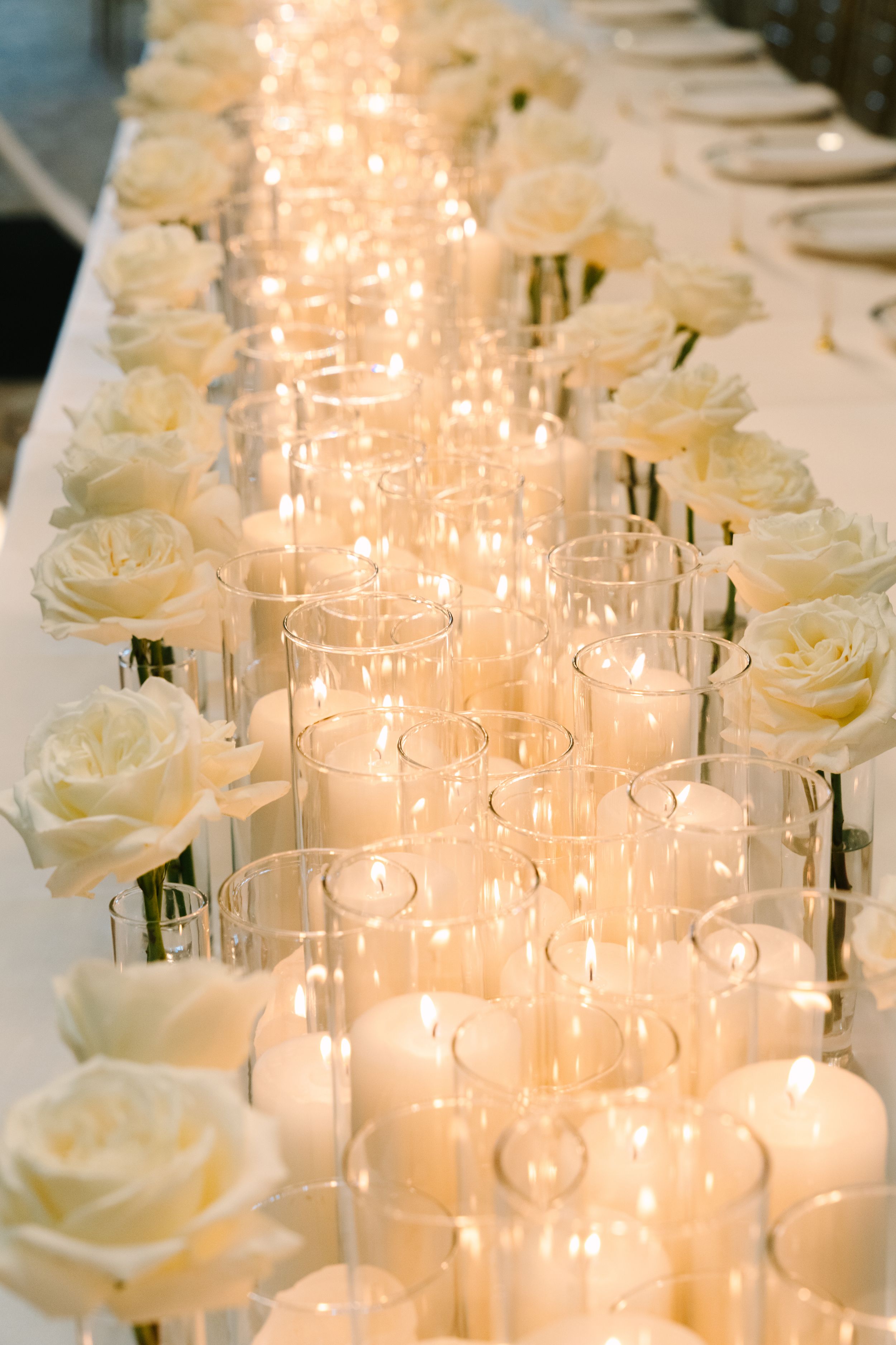 Elegant wedding table centerpiece with white roses and glowing candles in glass holders creating a romantic ambiance.
