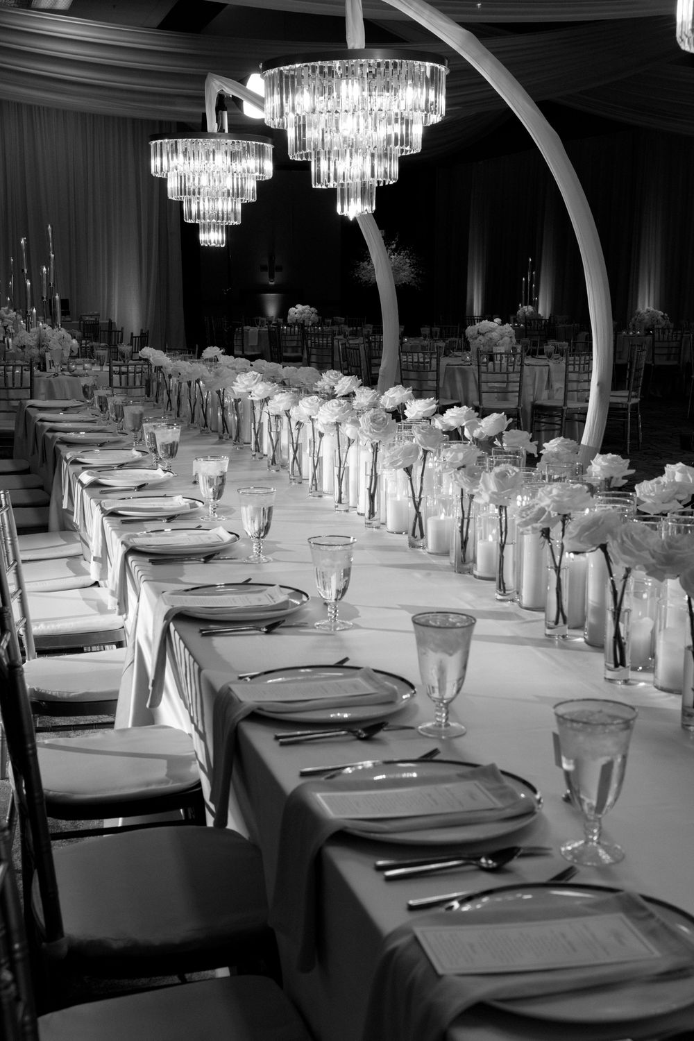 Elegant black and white banquet hall with long dining tables, crystal chandeliers, floral centerpieces, and formal place settings.