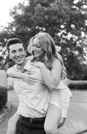 A romantic black and white portrait of a couple laughing together outdoors with natural bokeh lighting in the background.