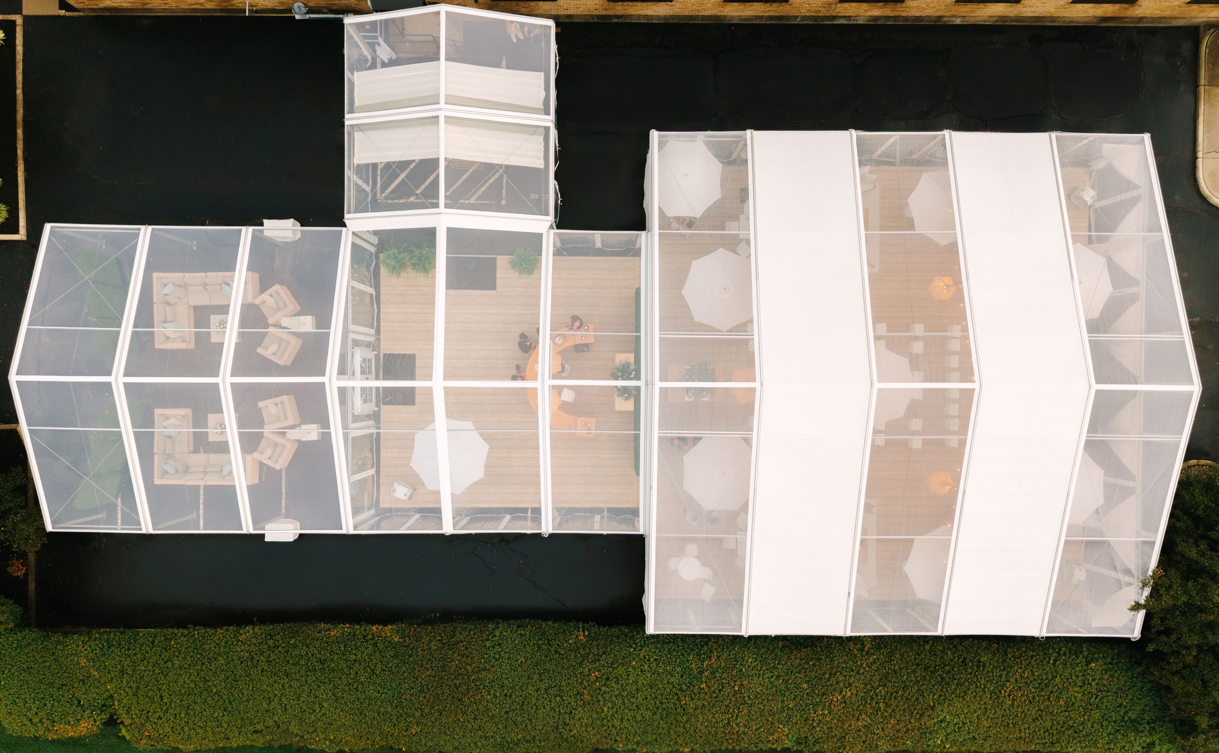 Aerial view of a transparent glass greenhouse structure with white panels and seating areas on a dark surface.