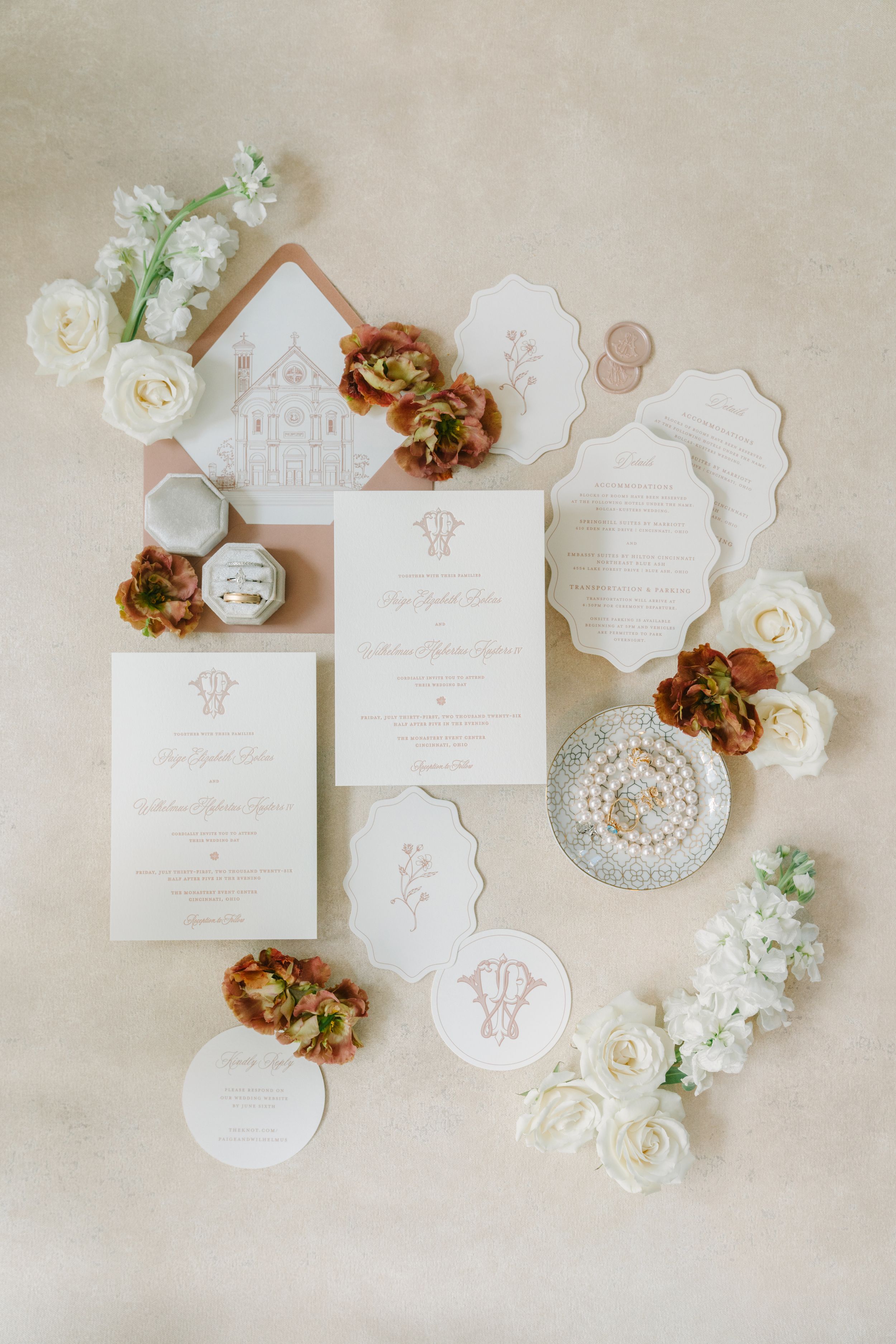 Elegant wedding invitation suite with floral accents, pearl jewelry, and rose gold envelopes on a neutral background.