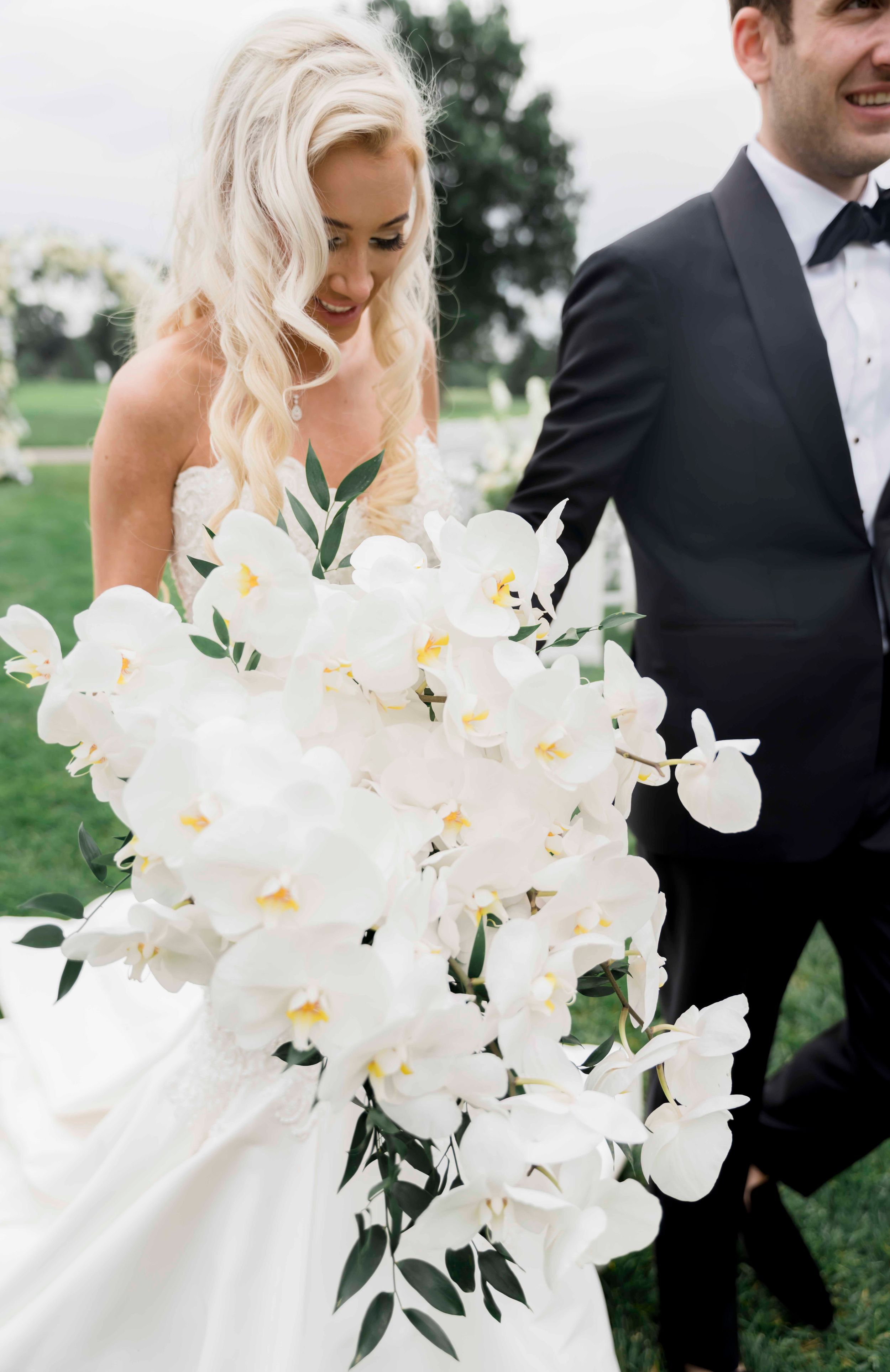 A bride holds a stunning cascading bouquet of white phalaenopsis orchids and greenery while wearing a strapless wedding gown.