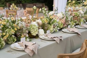 Elegant table settings with blush pink napkins and floral centerpieces at an outdoor wedding reception.