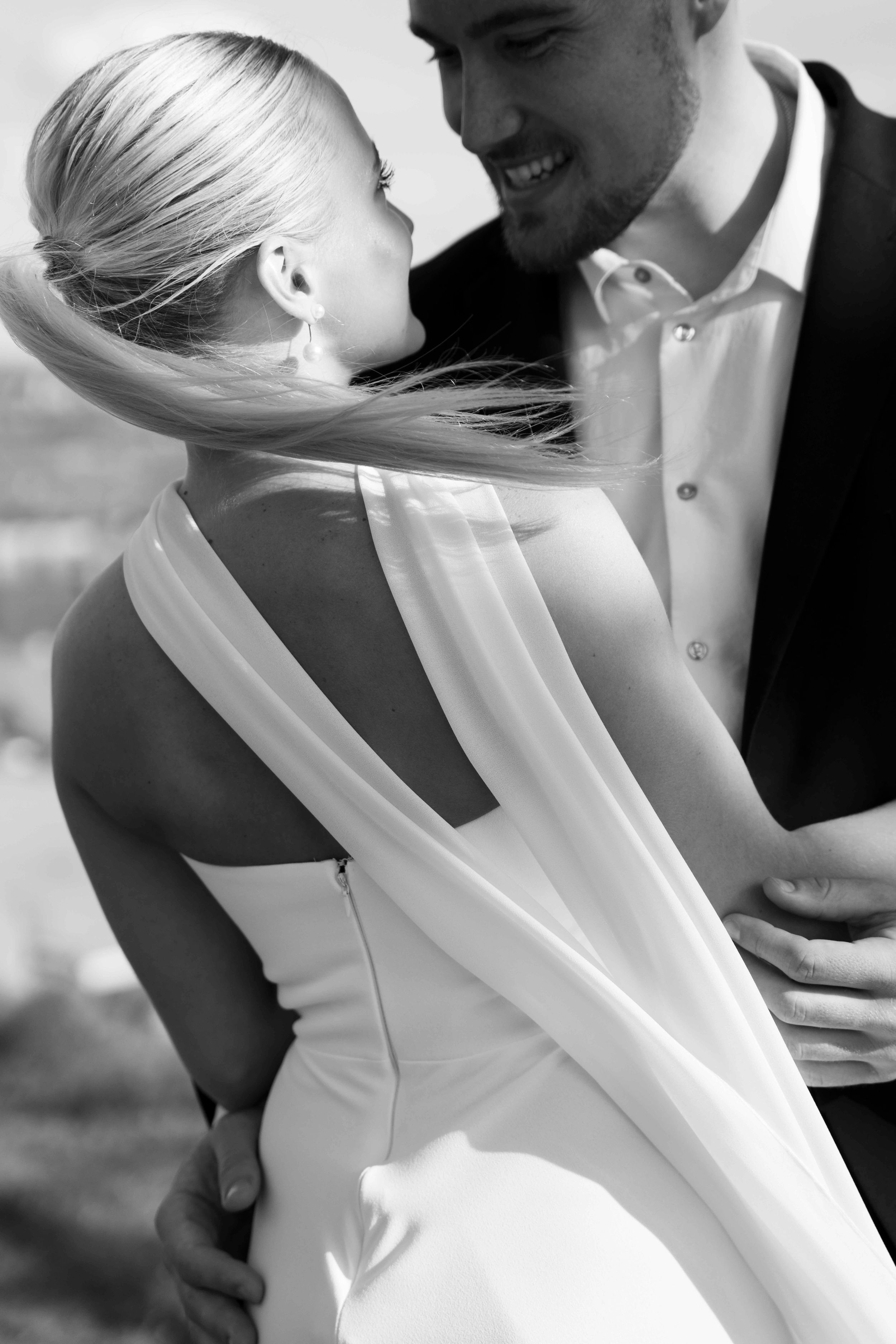Black and white wedding photo showing happy couple in intimate romantic pose with bride in sleeveless gown and sheer veil.