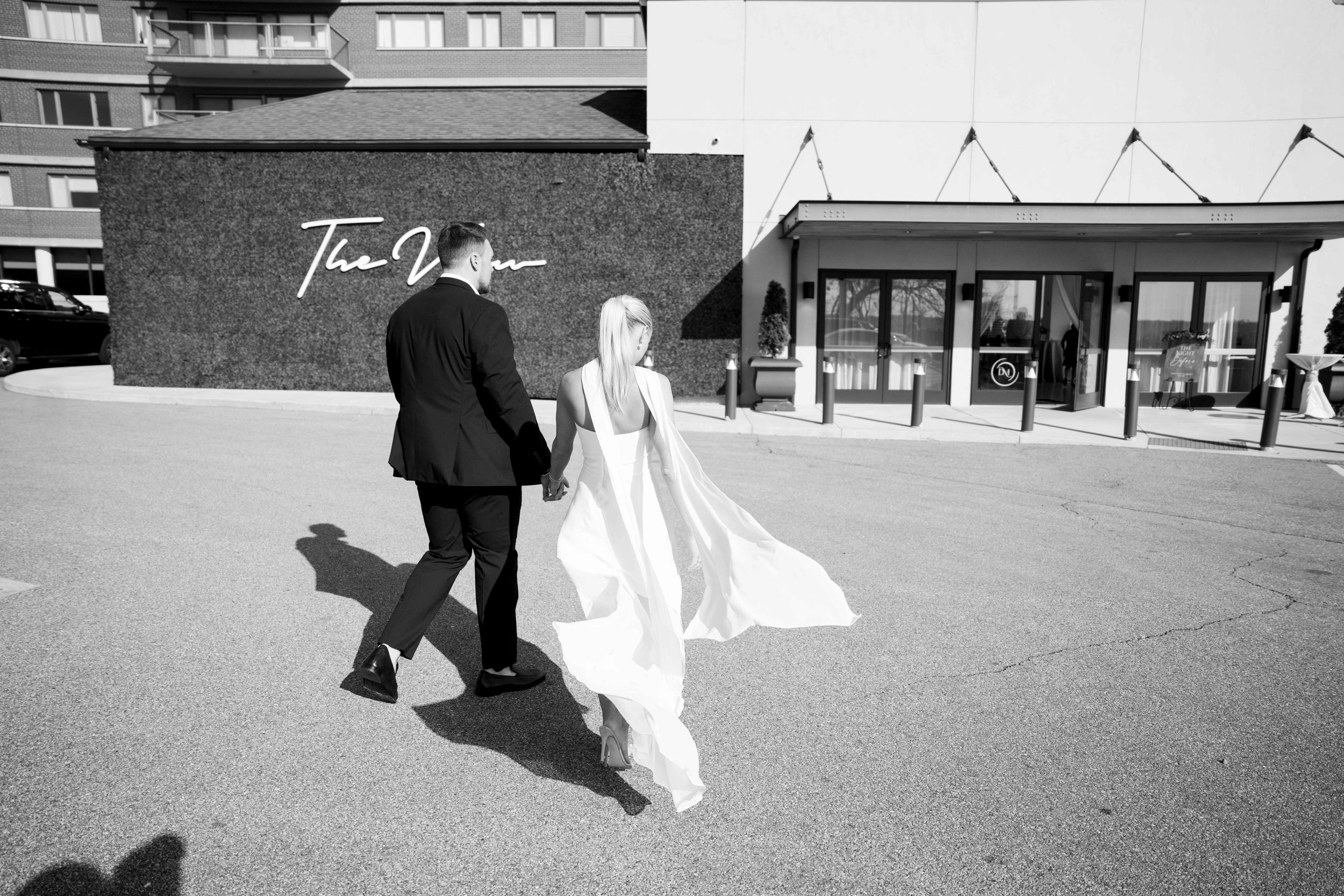 Black and white photo of a couple walking on a sunny day, with the bride's dress flowing in the wind.