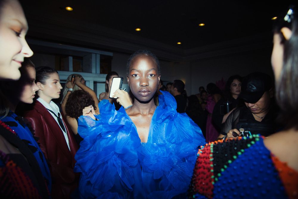 Backstage moment with model in bold blue feathered look surrounded by crowd | Fashion Photography by Dario Hudon-Verrelli, Le Café Studio