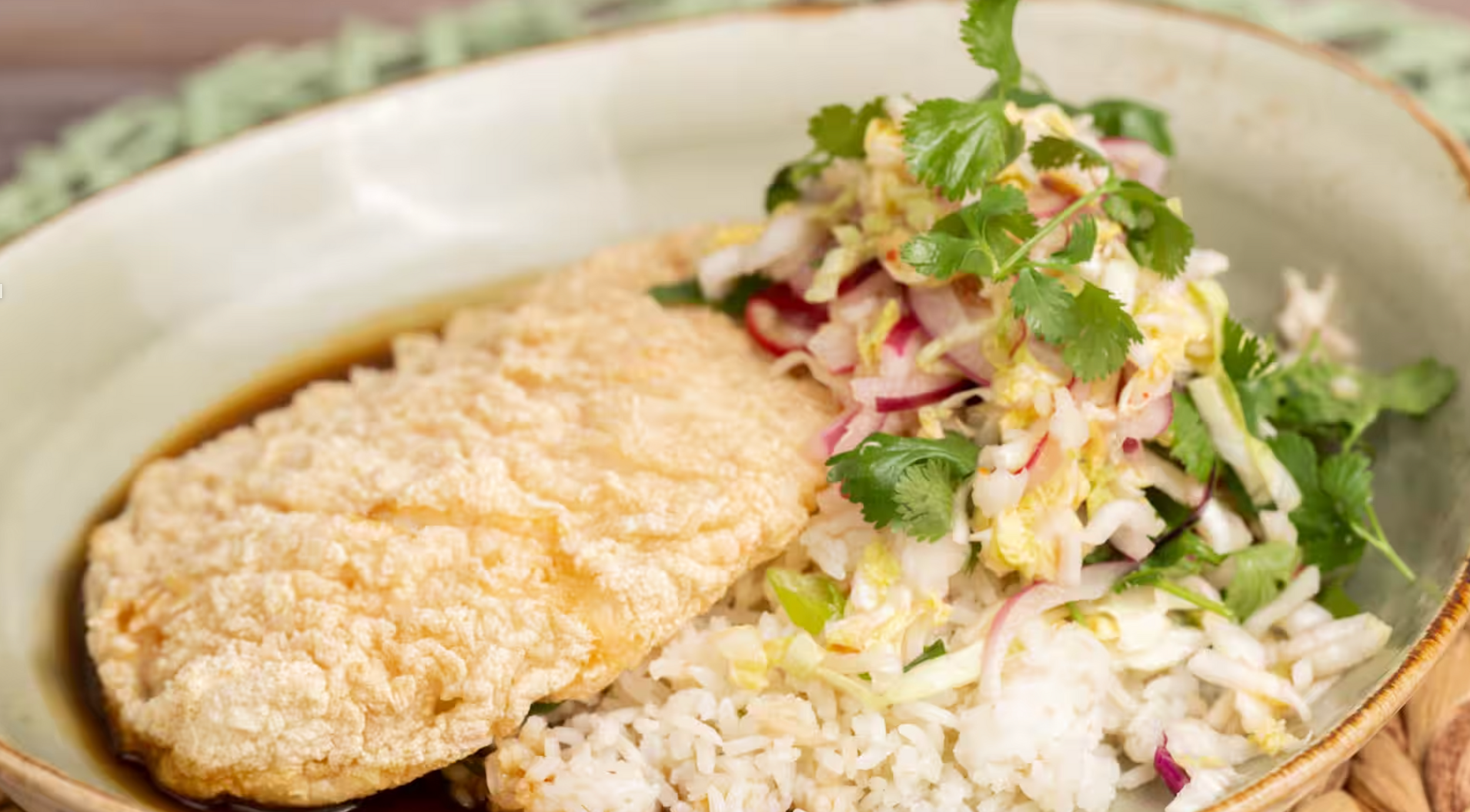 Fish tacos topped with fresh cilantro, shredded cabbage and sauce on white corn tortillas arranged on a serving platter.