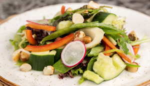 Fresh green salad with sliced cucumbers, radishes, carrots and macadamia nuts served on a white ceramic plate.