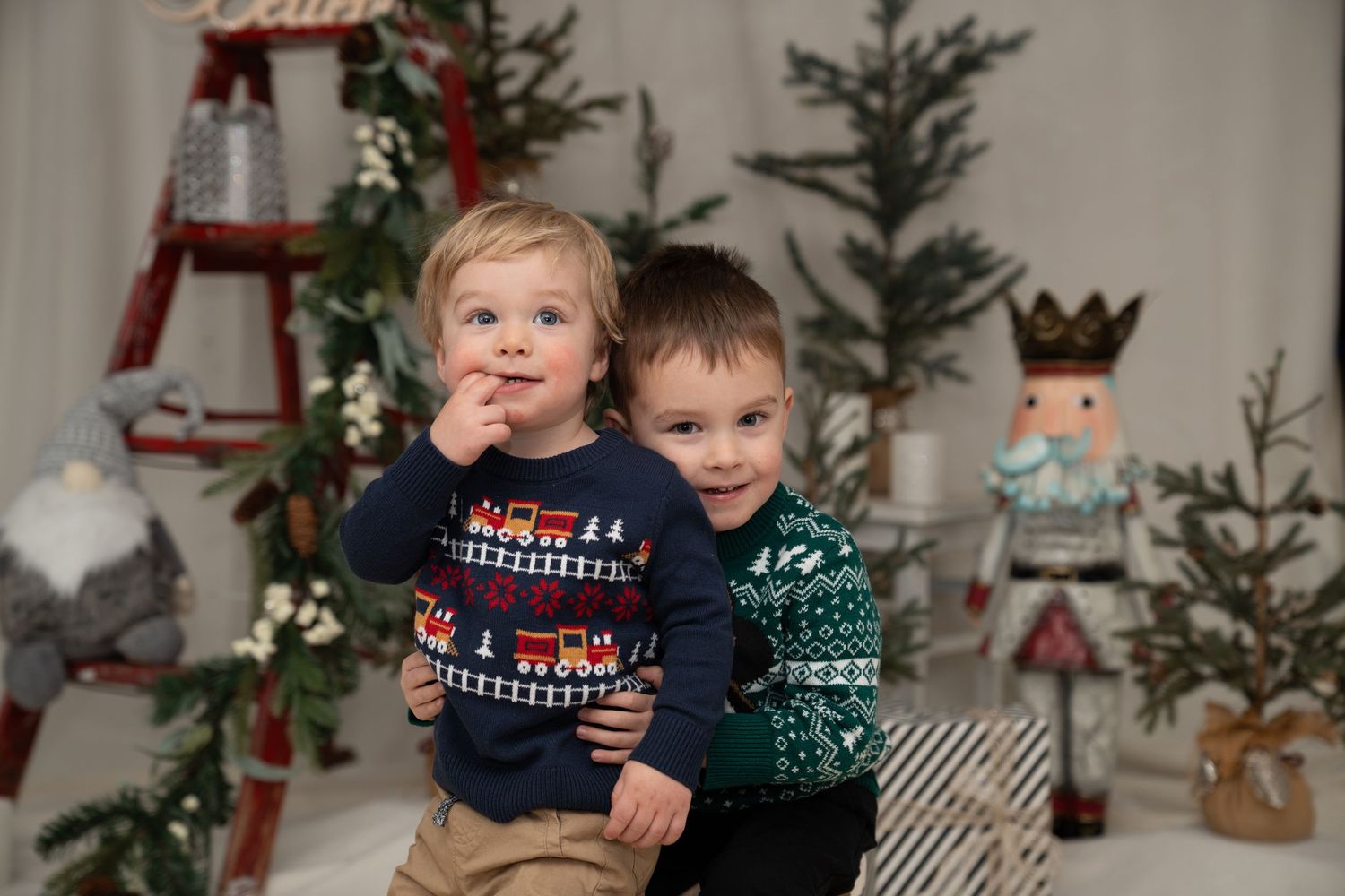 Children wearing festive holiday sweaters posing near Christmas decorations.