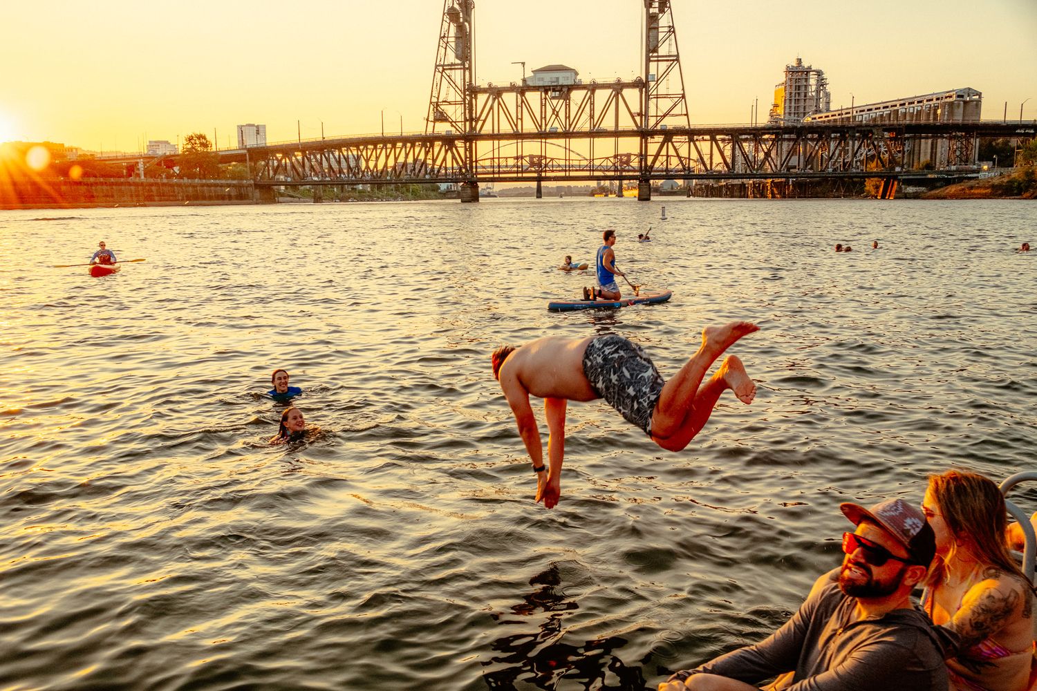 Person performing acrobatic flip over water at sunset near bridge in Portland.