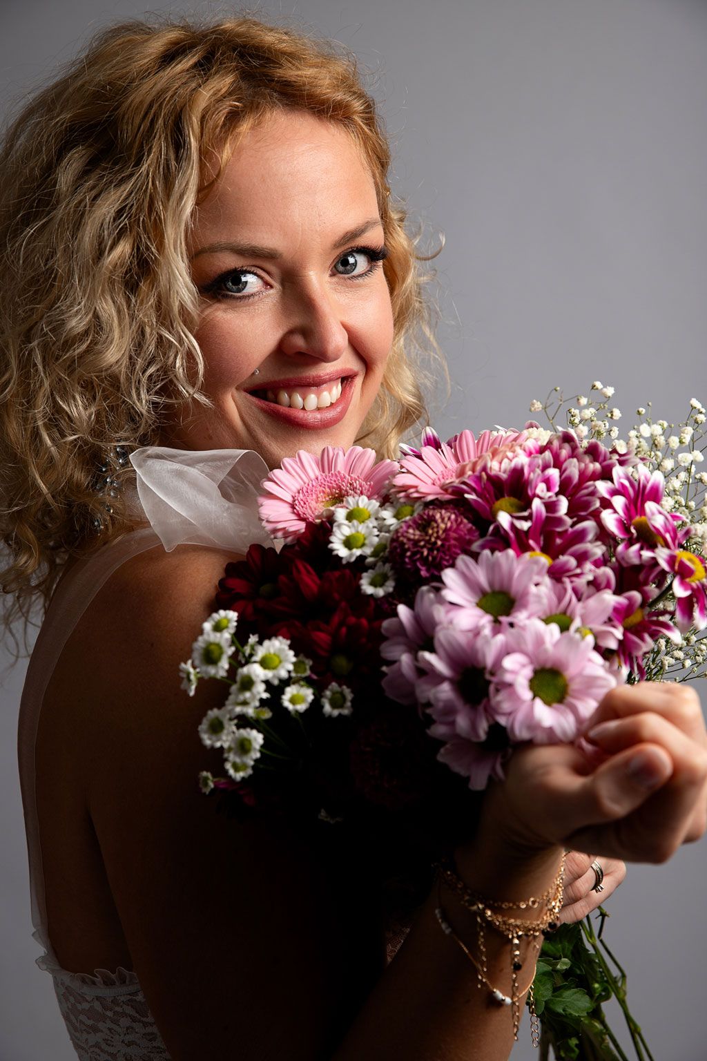 Une femme joyeuse en blanc tient un bouquet de fleurs roses et  sur fond sombre.