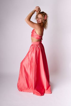 Mannequin posant dans une élégante tenue deux pièces corail, avec une jupe longue fluide et un top bandeau, sur un fond clair en studio.