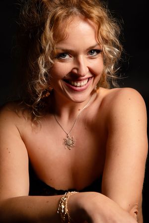 Portrait en gros plan en studio mettant en valeur une épaule, un collier et un bracelet sur un fond sombre avec un éclairage dramatique.