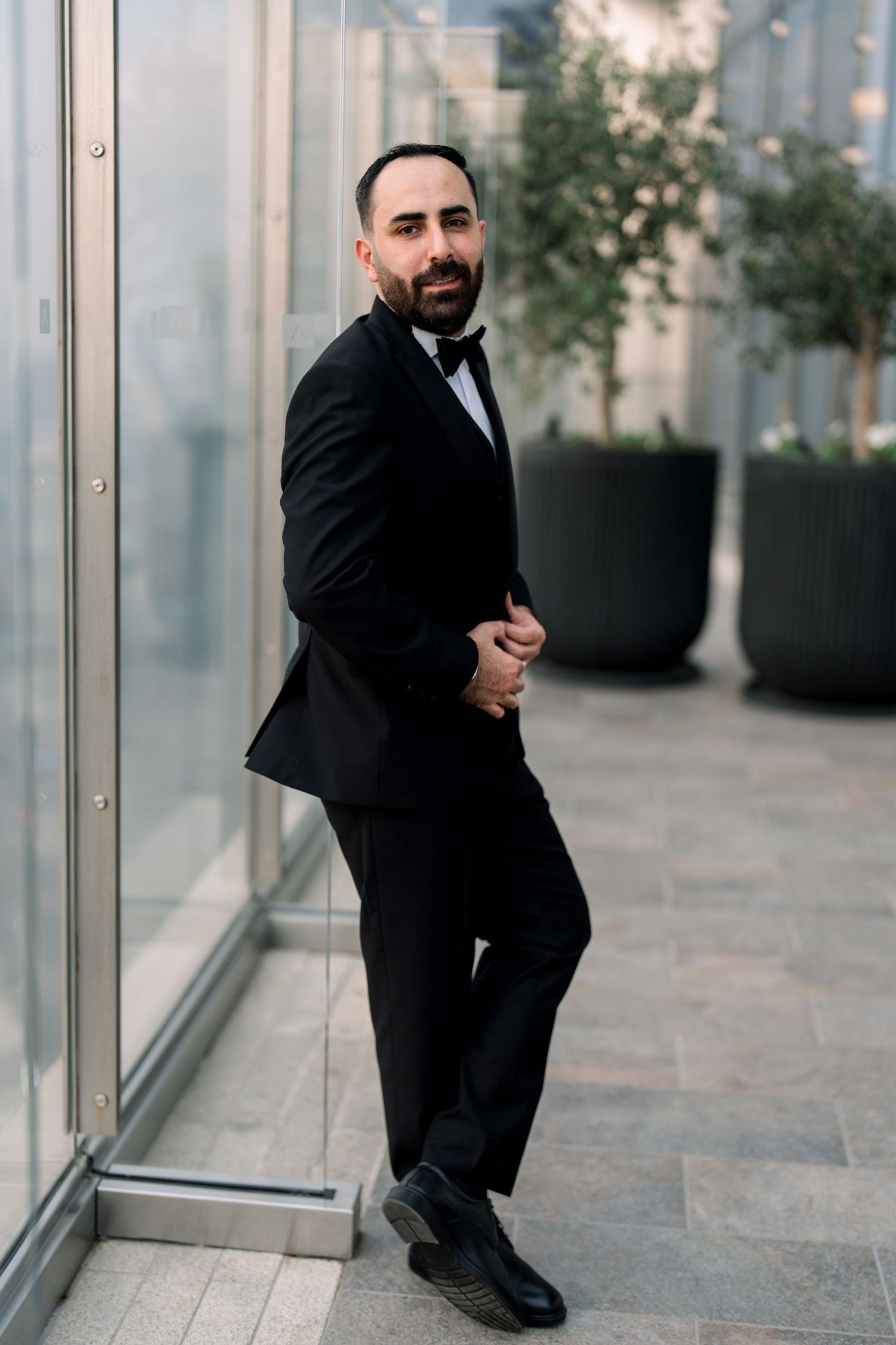 Business professional in dark suit crouches down in modern office hallway with glass windows and stone flooring.