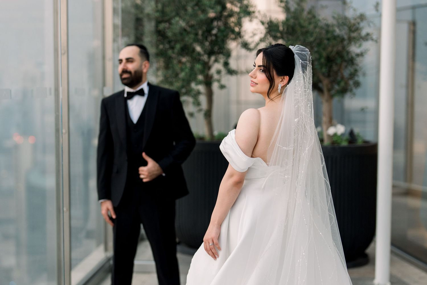 Elegant wedding party poses in formal attire against a modern glass building backdrop.