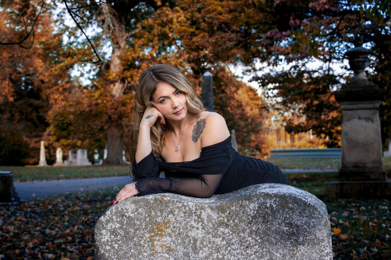Girl in black dress posed on a headstone at Spring Grove Cemetery featuring moody gothic Halloween portrait photography and cinematic outdoo