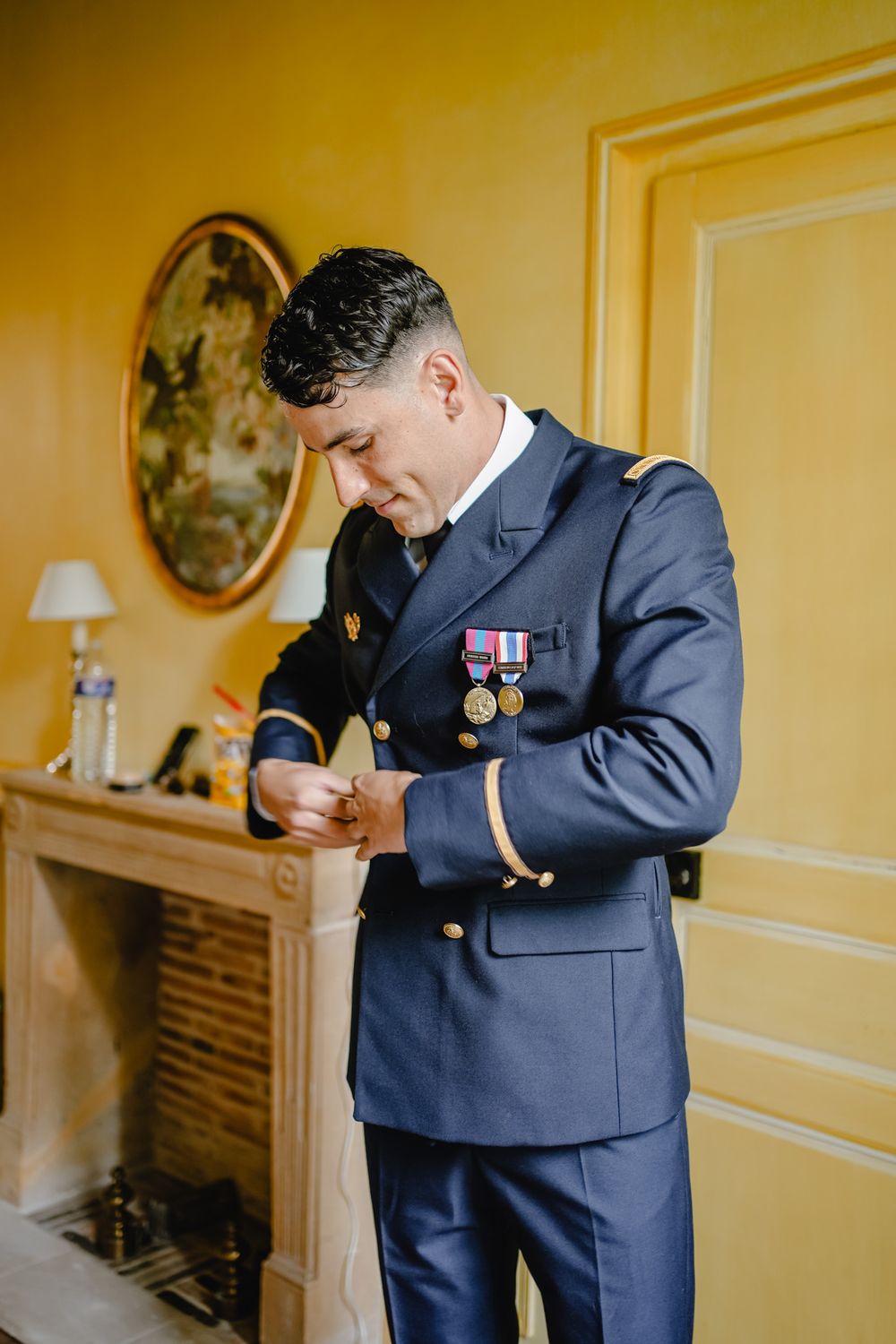 Military dress uniform details being adjusted in yellow-toned room.