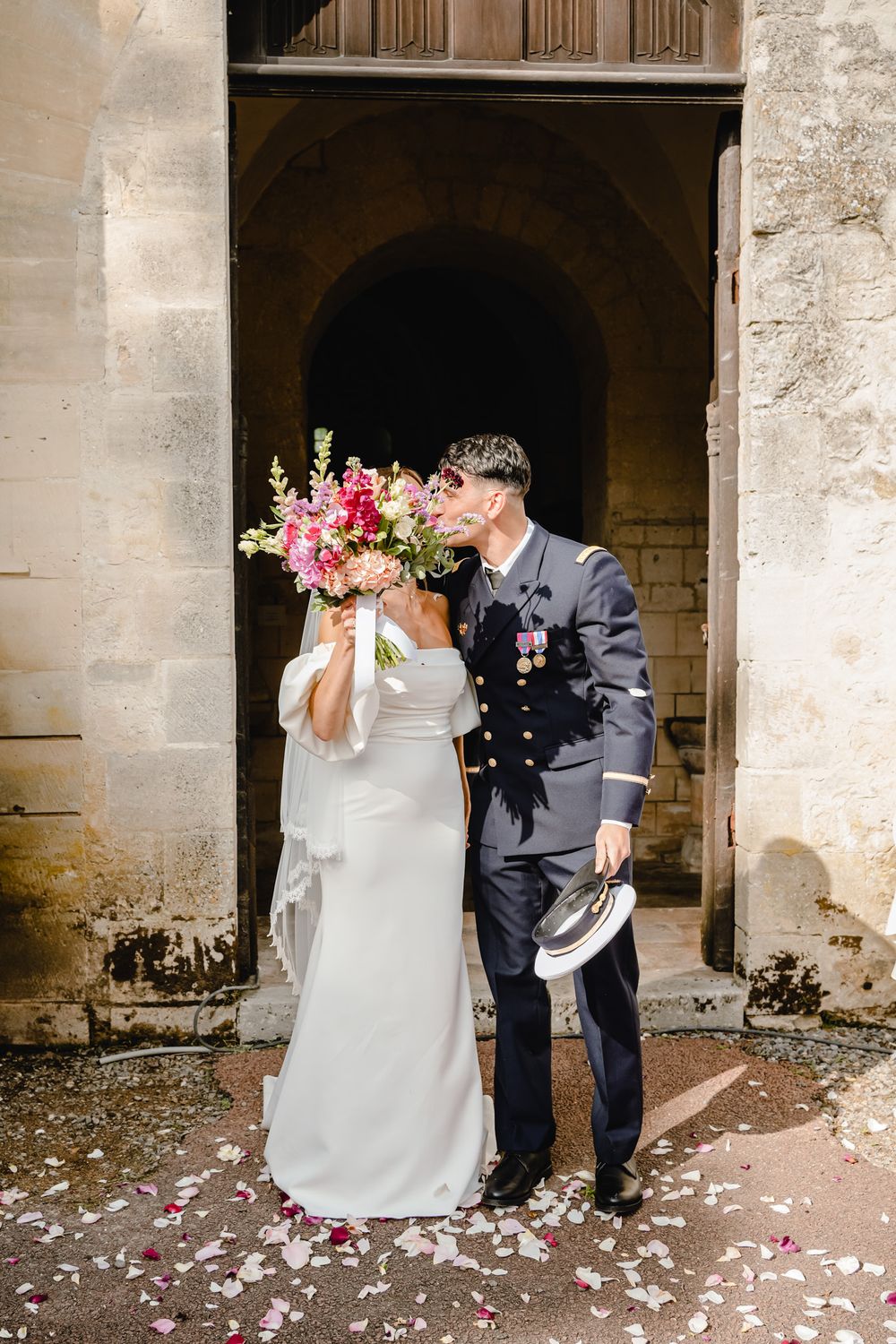 Wedding couple showered with flower petals under stone archway.