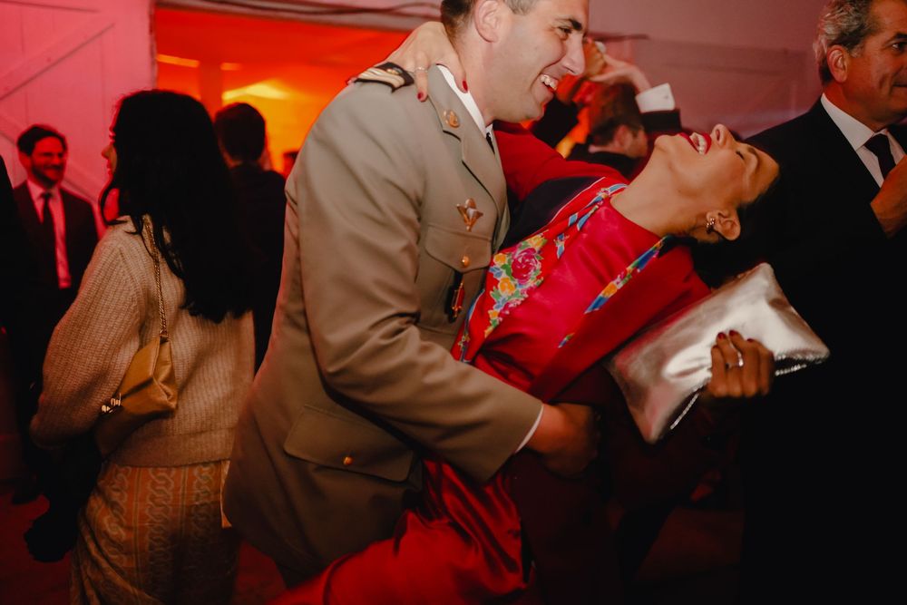 Couples dancing and celebrating at wedding reception with red ambient lighting.
