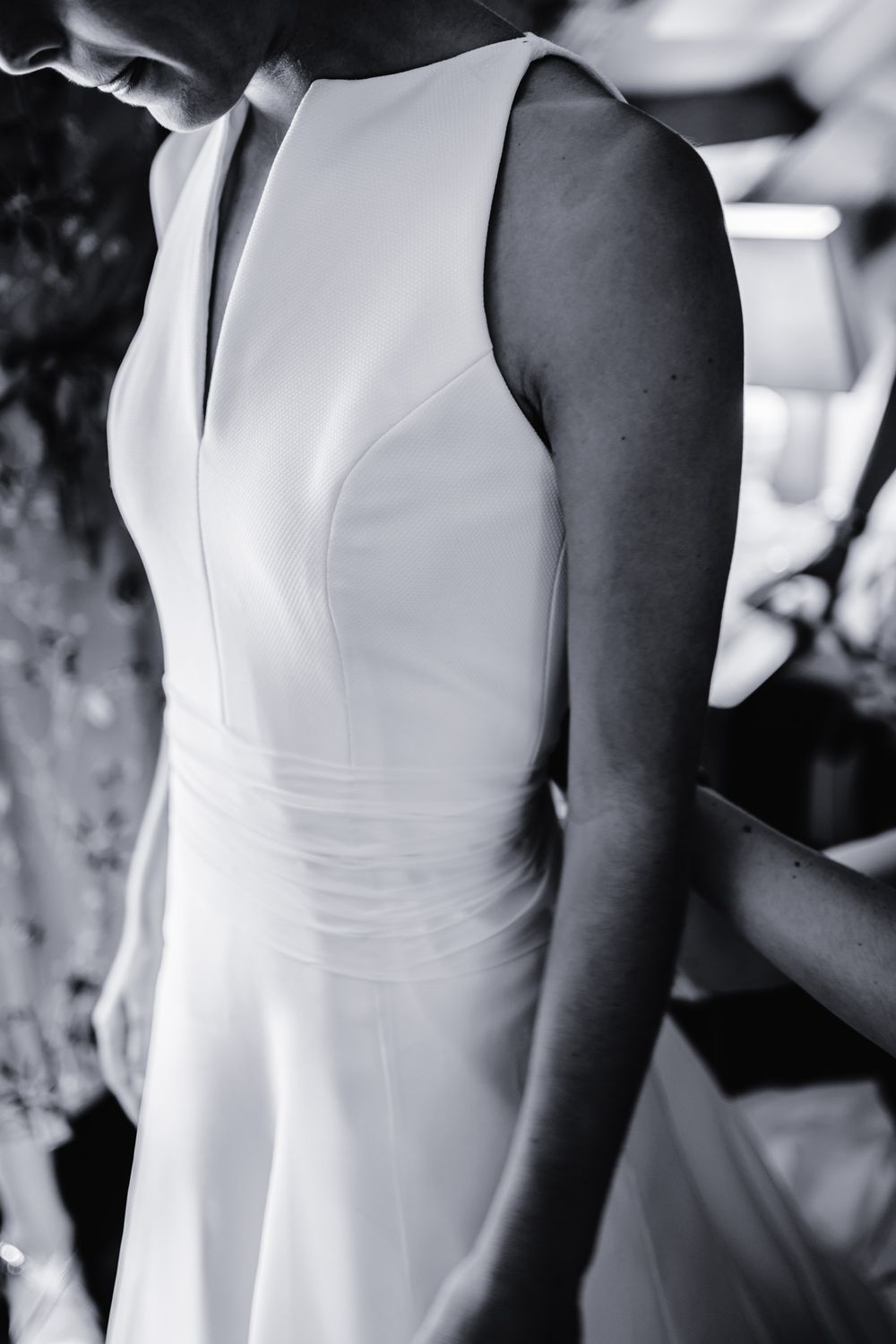 Elegant white sleeveless wedding dress details shown in black and white photography.