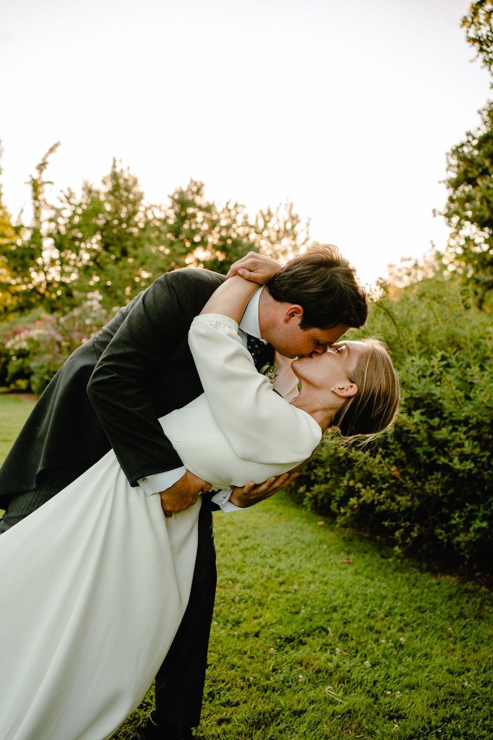 Romantic sunset dip kiss in garden setting with white wedding dress flowing.