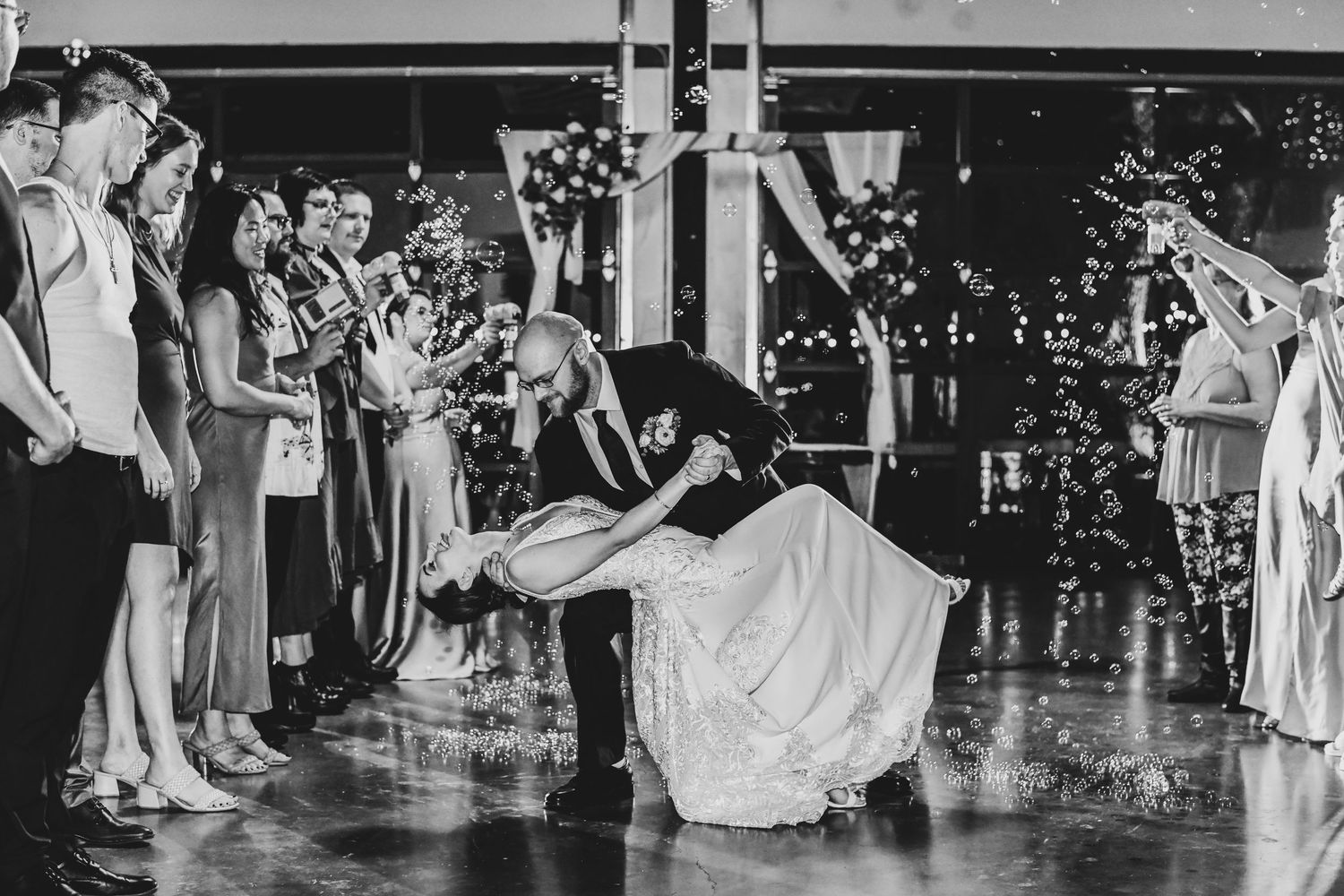a romantic wedding send off where a groom dips his bride as their friends and family blow bubbles around them