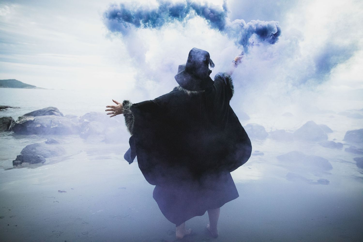 A silhouetted figure in a dark coat stands against a cloudy sky background in a panoramic composition.