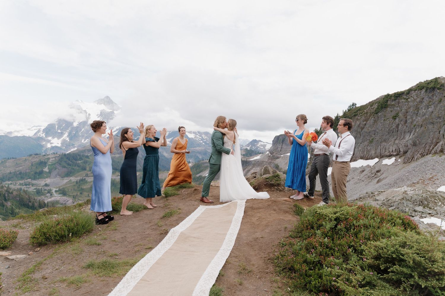 A wedding ceremony takes place on a mountain path with dramatic snow-capped peaks in the background.