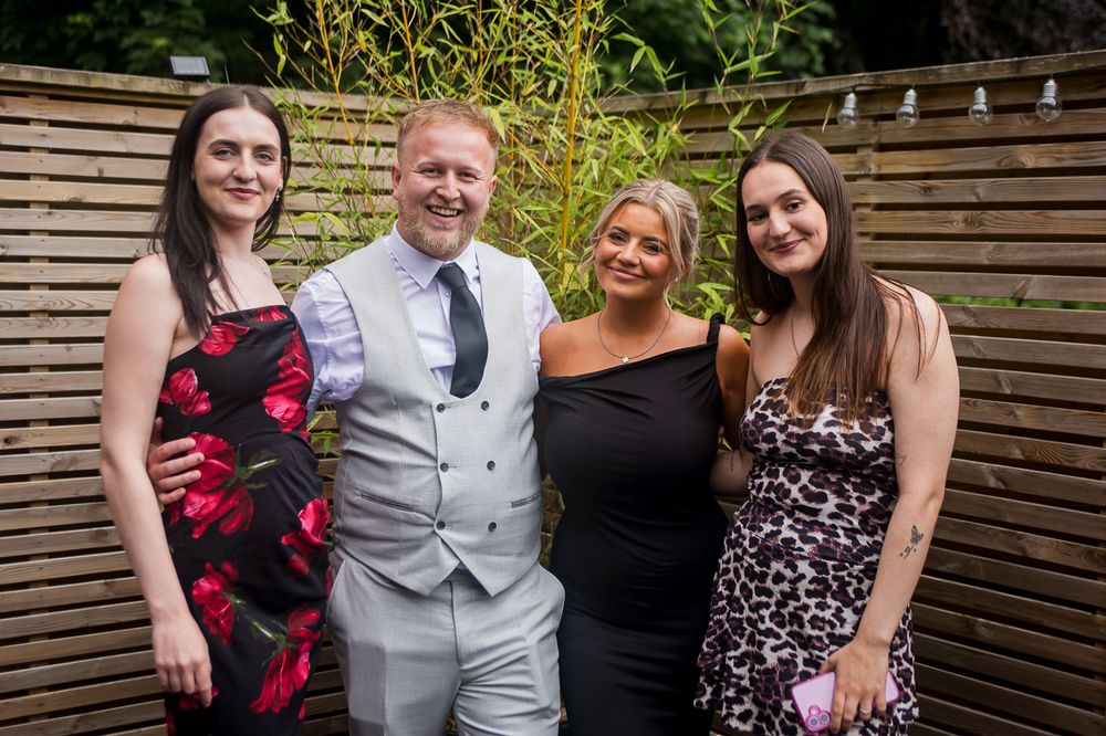 Group photo at outdoor garden party with wooden fence backdrop and string lights.