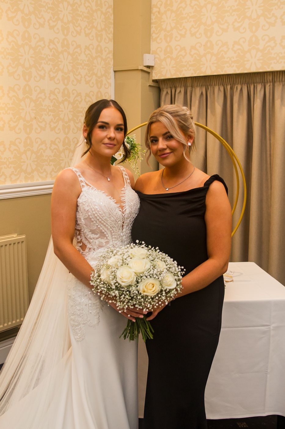 Indoor wedding portrait with cream wallpaper background and white floral bouquet.